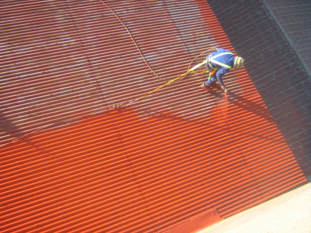 Roof Painting in Progress Worker actively applying paint on the roof surface, showing the ongoing painting process