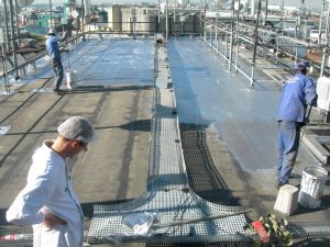 Worker applying a silver reflective sealant to the roof surface to protect and waterproof the structure