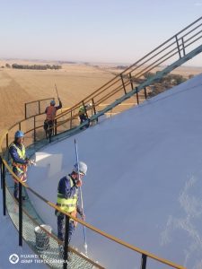Worker performing painting on the rooftop of a silo or similar industrial structure, showcasing expertise in high-elevation projects