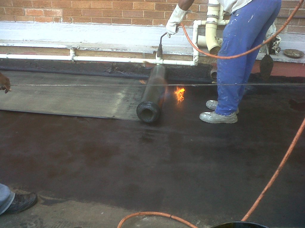Worker using a torch to apply torch-on bitumen membrane on a roof for waterproofing purposes